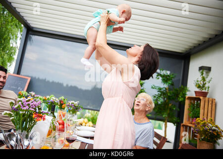 Donna matura il sollevamento baby nipote a pranzo di famiglia sul patio Foto Stock