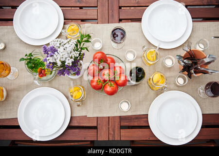 Vista aerea della tavola preparata con fiori e pomodori a grappolo per pranzo sul patio Foto Stock