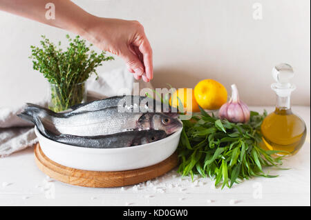 Sale donna pesce crudo prima della cottura. Il pesce fresco e gli ingredienti sul bianco tavolo in legno. Foto Stock