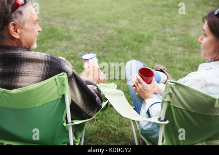 Coppia matura in seduta camping sedie, azienda tazze di stagno, vista posteriore Foto Stock