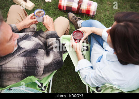 Coppia matura in seduta camping sedie, tenendo le tazze di tè, vista in elevazione Foto Stock