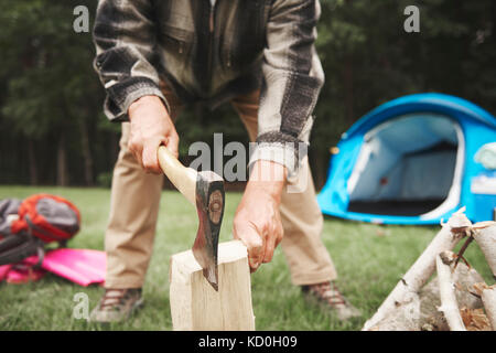 Uomo accanto a tenda, utilizzando ax per tritare legna da ardere, metà sezione Foto Stock