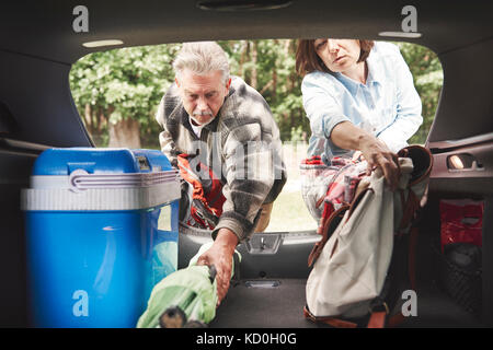 Coppia matura la rimozione di attrezzature per il campeggio dal bagagliaio della vettura Foto Stock