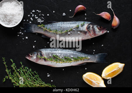 Due nuove materie pesci con sale e gli ingredienti sulla pietra nera tabella Foto Stock