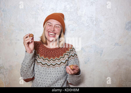 Ritratto di donna che indossa il ponticello e berretto lavorato a maglia, tenendo le noci, ridendo Foto Stock