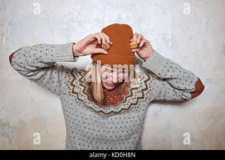 Ritratto di donna che indossa il ponticello e berretto lavorato a maglia, tenendo le noci per la sua testa, ridendo Foto Stock