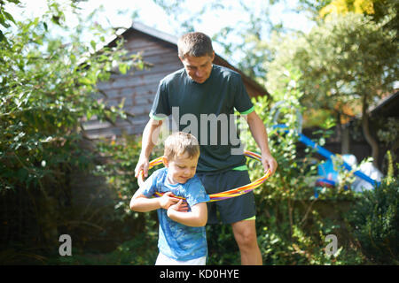 Ragazzo e padre giocando con il cerchio di plastica in giardino Foto Stock