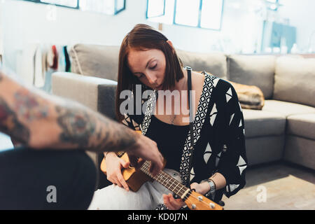 Giovane donna in appartamento a imparare a suonare ukulele dal fidanzato Foto Stock