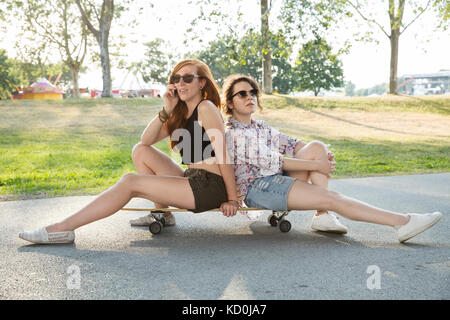 Ritratto di due giovani donne all'aperto, seduti su skateboard Foto Stock