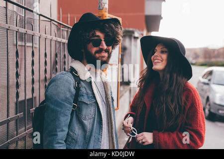 Coppia giovane in piedi alla fermata bus, ridendo Foto Stock