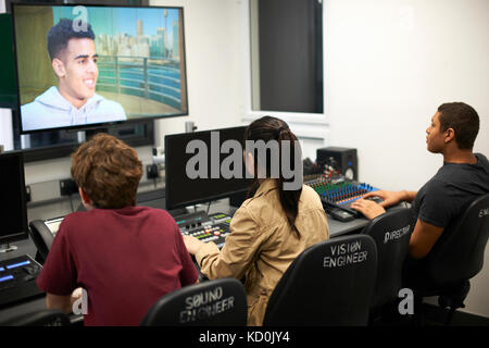 Giovane maschio e femmina studenti del college a miscelazione a scrivania guardando sullo schermo del televisore Foto Stock