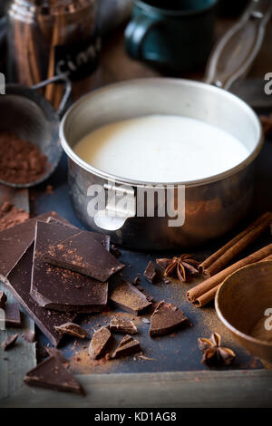 La preparazione di cioccolata calda - una piccola pentola di latte, polvere di cacao, cioccolato fondente bar, cannella e anice stellato Foto Stock