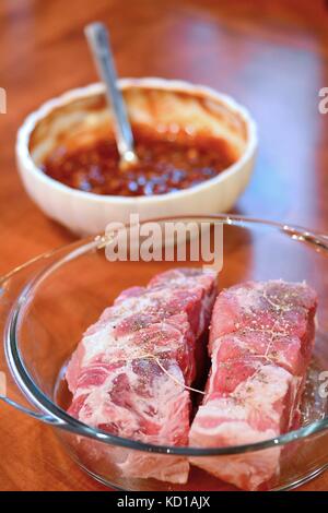 Due pezzi di carne di maiale cruda colli e ciotola con il piccante marinata su una scrivania. Foto Stock