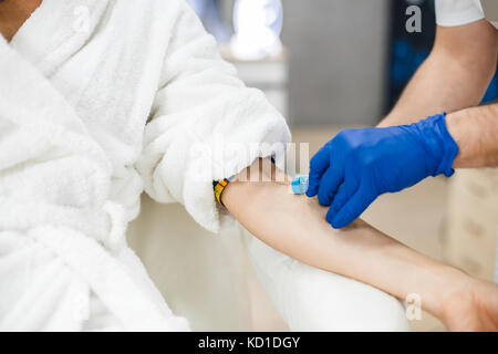 Vista ravvicinata del medico maschio la raccolta di sangue dal paziente. immagine ritagliata della prova di sangue dalla vena con bella giovane donna dal medico maschio. Foto Stock