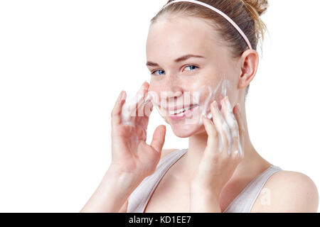 Adolescente skincare. sorridente bella redhead teen ragazza con le lentiggini e gli occhi blu usando detergente schiumogeno. viso lavaggio concetto isolato Foto Stock