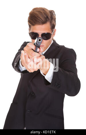Agente segreto indossando occhiali da sole mirando con la pistola verso la telecamera Foto Stock