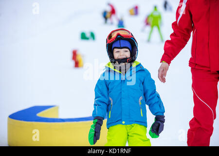 Felice giovane ragazzo in piedi accanto a istruttore sulla pista da sci in area per bambini Foto Stock