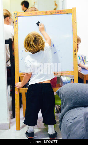 Un bambino biondo di 2-3 anni disegna su una lavagna bianca in un asilo Foto Stock