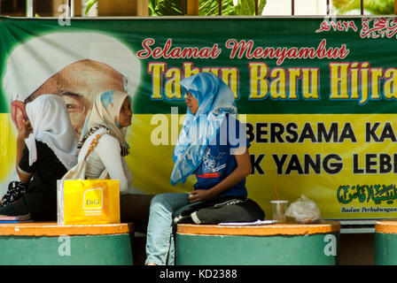 In corrispondenza di un Autobus Alloggio in Kota Bharu, stato di Kelantan, Malay le donne musulmane attendere accanto a un cartellone per celebrare l'annuale Hijra o pellegrinaggio alla Mecca. Foto Stock