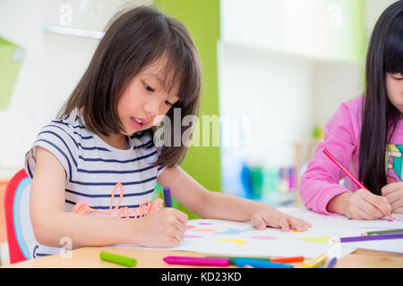 Ragazza in età prescolare kid Disegno con matite colorate su carta bianca sulla tavola in aula con gli amici e il maestro,kindergarten concetto di istruzione Foto Stock