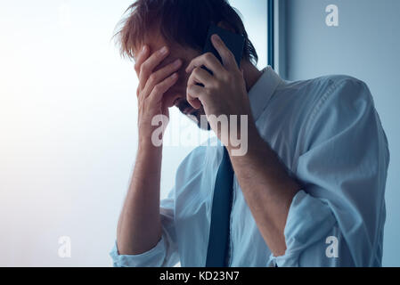 Imprenditore in piedi accanto alla finestra di ufficio e utilizza lo smartphone. business comunicazione tramite messaggi sms o mobile apps. persona d'affari ricevuto cattive Foto Stock