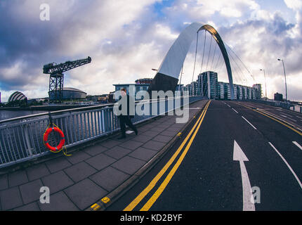 Uomo che cammina al di sopra del ponte Squinty a Glasgow, aka il Clyde Arc, con la gru Finnieston , SSE Idro e SECC Armadillo in background Foto Stock