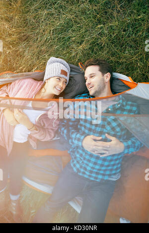 Coppia giacendo in tenda, teste al di fuori della tenda, sorridente, vista aerea Foto Stock