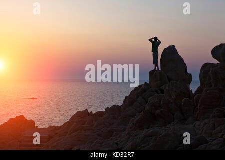 Silhouette di uomo sulle rocce che guarda lontano al tramonto sul mare, Olbia, Sardegna, Italia Foto Stock