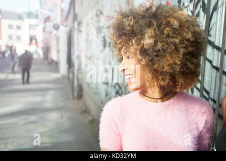 Giovane donna all'aperto che guarda lontano, sorridente Foto Stock