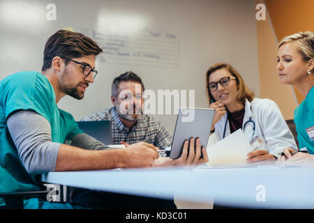 Team di personale medico avente riunione mattutina in sala riunioni. I medici e gli infermieri guardando digitale compressa. Foto Stock