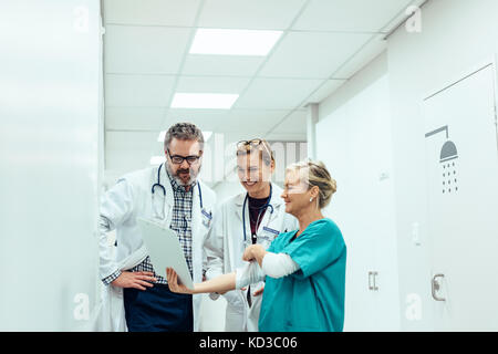 Femmina matura infermiera mostra appunti per i medici in corridoio. Team di medici guardando il rapporto medico mentre in piedi nel corridoio dell'ospedale. Foto Stock
