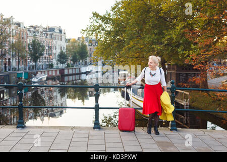 La donna con la valigia è in appoggio sul ponte della città di Amsterdam in autunno Foto Stock