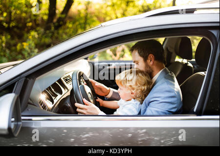 Uomo alla guida di una vettura con il suo piccolo figlio. toddler ragazzo seduto nel suo giro dei padri. Foto Stock