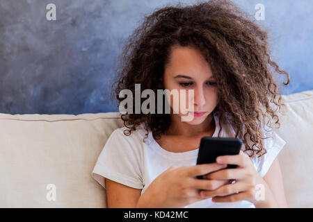 Capelli ricci teen ragazza scrive i messaggi sms a casa Foto Stock