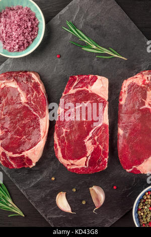 Tre fette di carne cruda su nero con il condimento Foto Stock