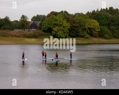 Le persone che stanno imparando a stand up paddle board su tittesworth serbatoio acqua, il Peak District, Staffordshire, Regno Unito Foto Stock