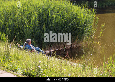 Uomo disteso su una riva del laghetto con canna da pesca Foto Stock