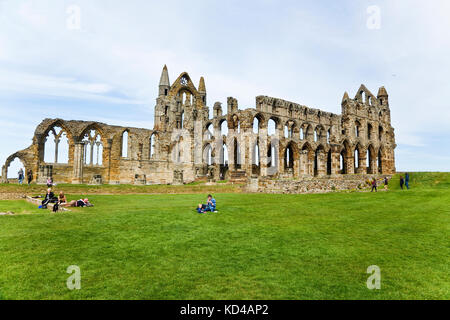 Vista delle rovine dell'abbazia sulla cima delle scogliere sopra Whitby Town con le persone che si siedono intorno sull'erba Foto Stock