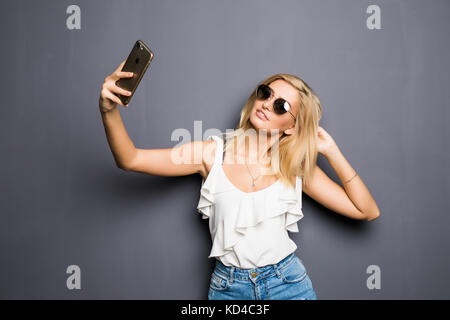 Donna felice in bicchieri con sorriso raggiante rendendo selfie e mostra v-sign Foto Stock