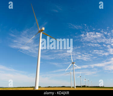 Allineamento delle turbine eoliche in mezzo a campi la generazione di elettricità da fonti rinnovabili dal vento. Foto Stock