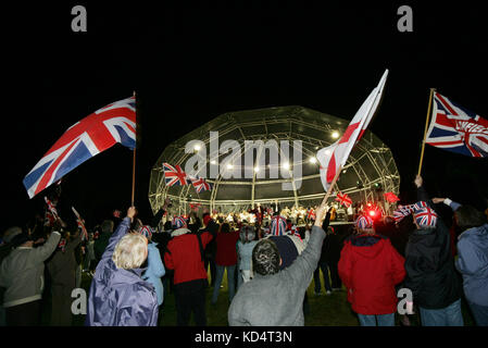 La gente sventolare la bandiera dell'Union Jack di notte davanti a una cupola illuminata stadio. Foto Stock