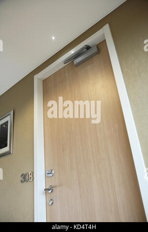 Primo piano di una moderna porta della camera d'hotel che mostra il chiudiporta e altri accessori per soddisfare le più recenti normative antincendio Foto Stock