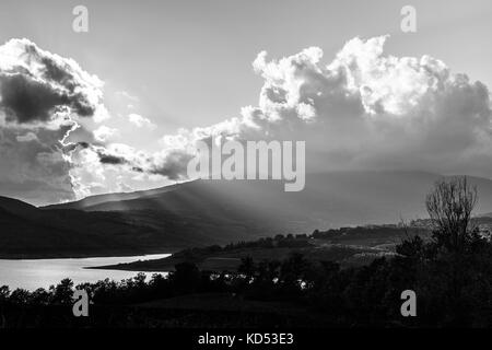 Bellissima vista del lago e delle colline, con raggi solari che filtrano attraverso le nubi e riflettendo su acqua Foto Stock