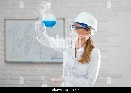 Giovani donne scienziato che lavora con sostanze chimiche liquide presso il laboratorio di indossare casco protettivo di occhiali e maschera. Foto Stock