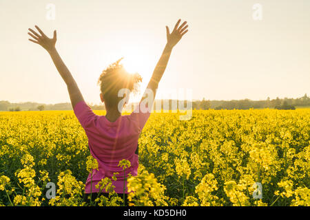 Razza mista African American Girl femmina donna giovane atleta runner adolescente in golden il tramonto o l'alba a braccia alzate celebrando nel campo del giallo flo Foto Stock