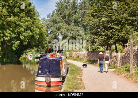 7 luglio 2017: Bradford on Avon, Somerset, Inghilterra, Regno Unito - giovane con il cane a camminare sul percorso di traino accanto a una fila di narrowboats ormeggiate lungo le rive di t Foto Stock