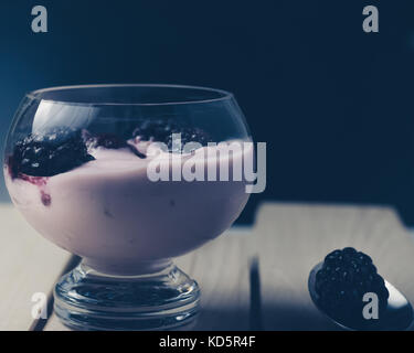 Yogurt alla frutta con more su una superficie in legno, vista frontale, sfondo scuro Foto Stock