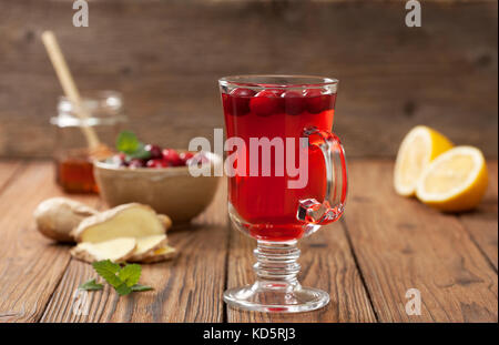 Mirtilli rossi con limone e zenzero drink in un bicchiere di vetro, mirtilli rossi in una ciotola, mezzo limone, fette di zenzero su un vecchio sfondo di legno Foto Stock