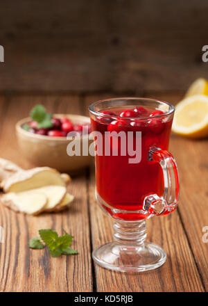 Mirtilli rossi con limone e zenzero drink in un bicchiere di vetro, mirtilli rossi in una ciotola, mezzo limone, fette di zenzero su un vecchio sfondo di legno Foto Stock