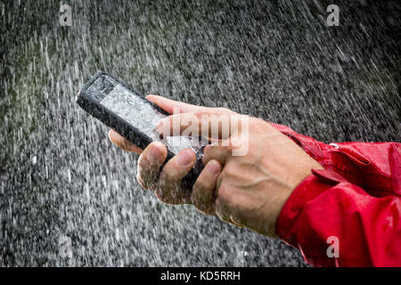 Un uomo con un telefono cellulare in una custodia impermeabile al di fuori sotto la pioggia Foto Stock